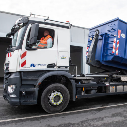 Ein GELSENDIENSTE Container wird von einem Fahrzeug abgerollt.