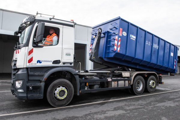 Ein GELSENDIENSTE Container wird von einem Fahrzeug abgerollt.