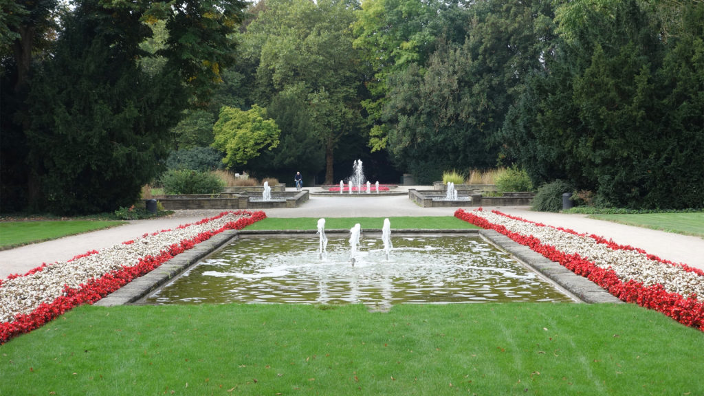 Blick auf die Wasserspiele im Stadtgarten, die von einer Wechselbepflanzung aus roten und weißen Blume eingerahmt sind.