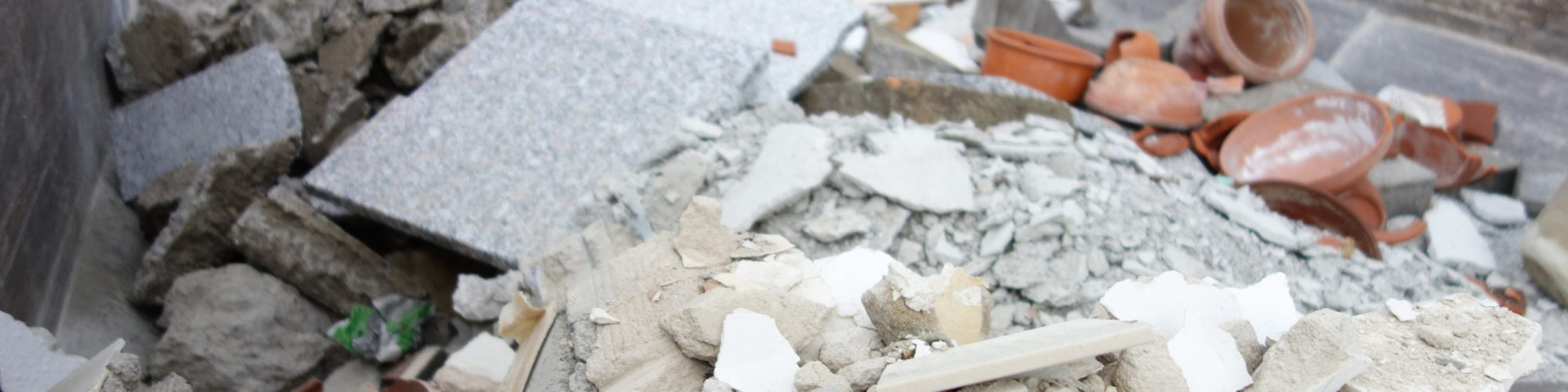 Großer Container gefüllt mit mineralischen Bauabfällen wie Mauersteinen und Granitplatten.