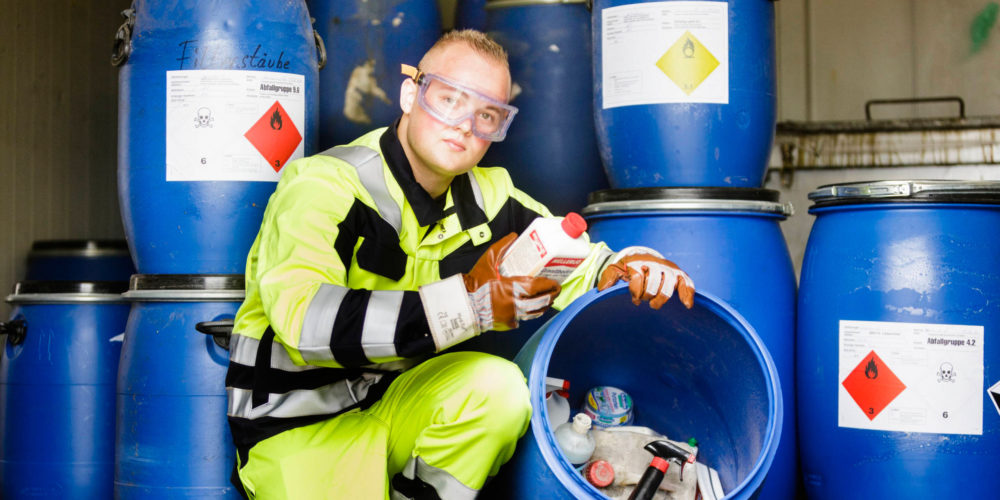 Eine Fachkraft für Kreislauf-und Abfallwirtschaft von GELSENDIENSTE sortiert Problemabfälle in blaue Behälter.